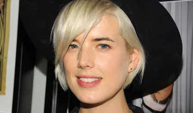 A person with short blonde hair and a black hat smiling at the camera.