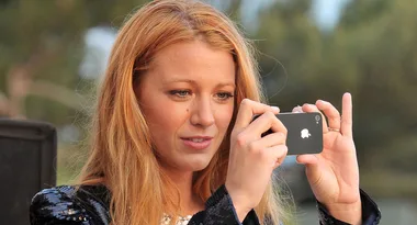 A woman with long hair uses an iPhone to take a photo outdoors.