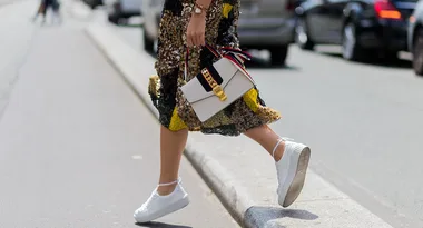 A woman in a sequined skirt walks on a street with white sneakers, holding a stylish handbag.