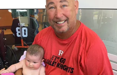 Man in red shirt holding a baby, smiling at the camera.