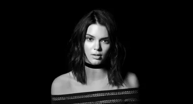 Woman with shoulder-length hair and choker in black-and-white portrait, off-shoulder top against a dark background.