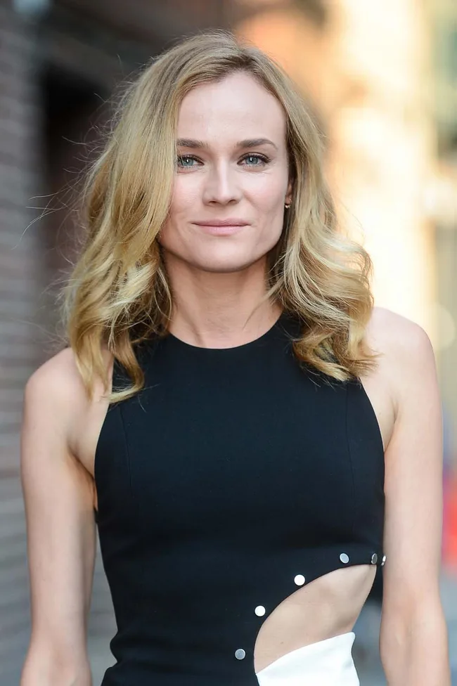 A person with blonde hair in a black sleeveless top stands outdoors, smiling slightly.