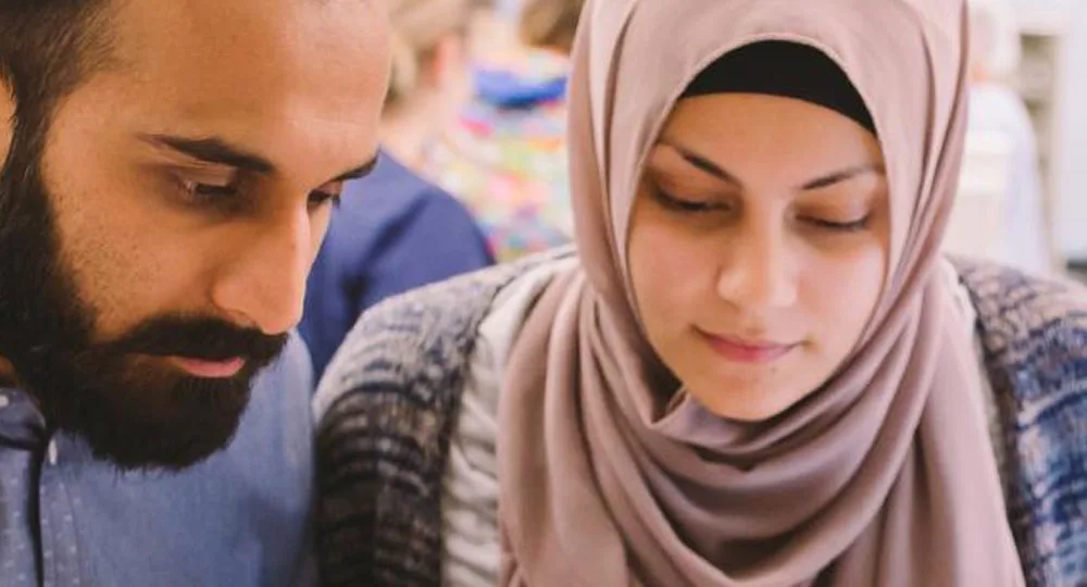 Two people, a man and a woman in a headscarf, are closely looking at something, possibly working together.