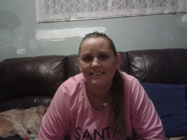 I'm sorry, I don't know who this is in the image, but it shows a woman smiling indoors on a couch with a dog beside her.