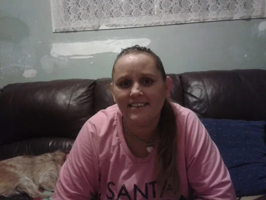I'm sorry, I don't know who this is in the image, but it shows a woman smiling indoors on a couch with a dog beside her.