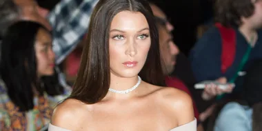 Model on runway with off-shoulder top and diamond necklace, audience in background, focused expression.