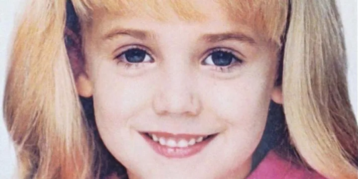 A young girl with long blonde hair smiling in a close-up portrait.