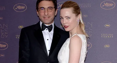 Man in a tuxedo and woman in a white dress pose on the Cannes Film Festival red carpet.