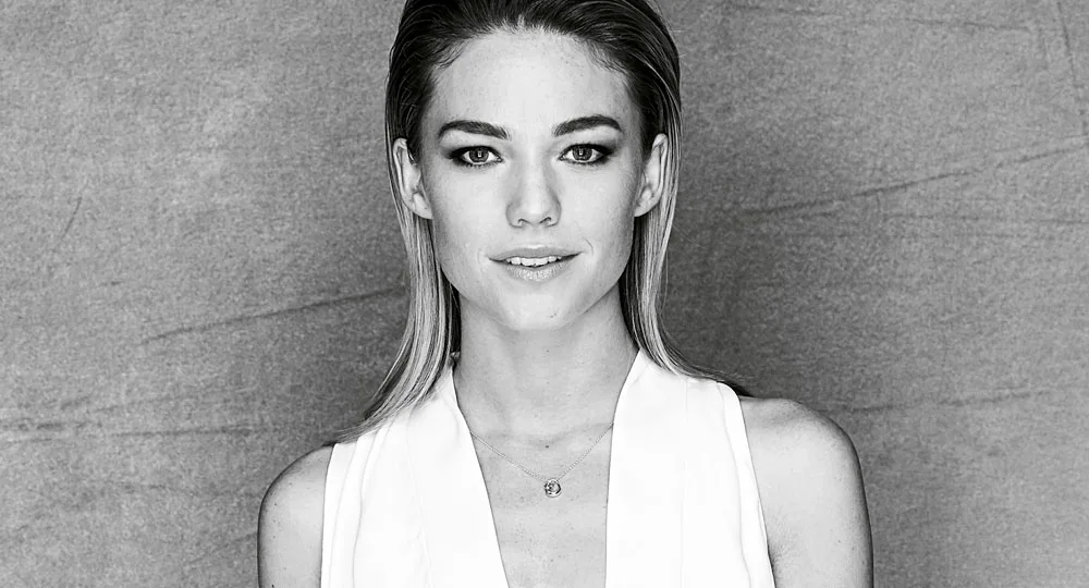 A black and white portrait of a woman with straight hair, wearing a white top against a textured background.