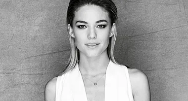 A black and white portrait of a woman with straight hair, wearing a white top against a textured background.