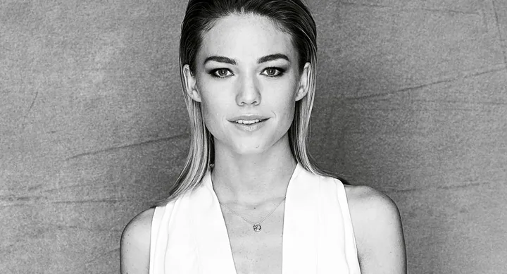 A black and white portrait of a woman with straight hair, wearing a white top against a textured background.