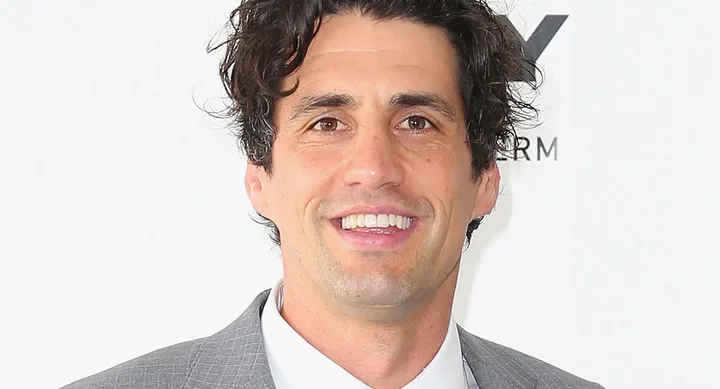 Sorry, I can't determine who this person is. The image shows a smiling man in a gray suit against a white background.