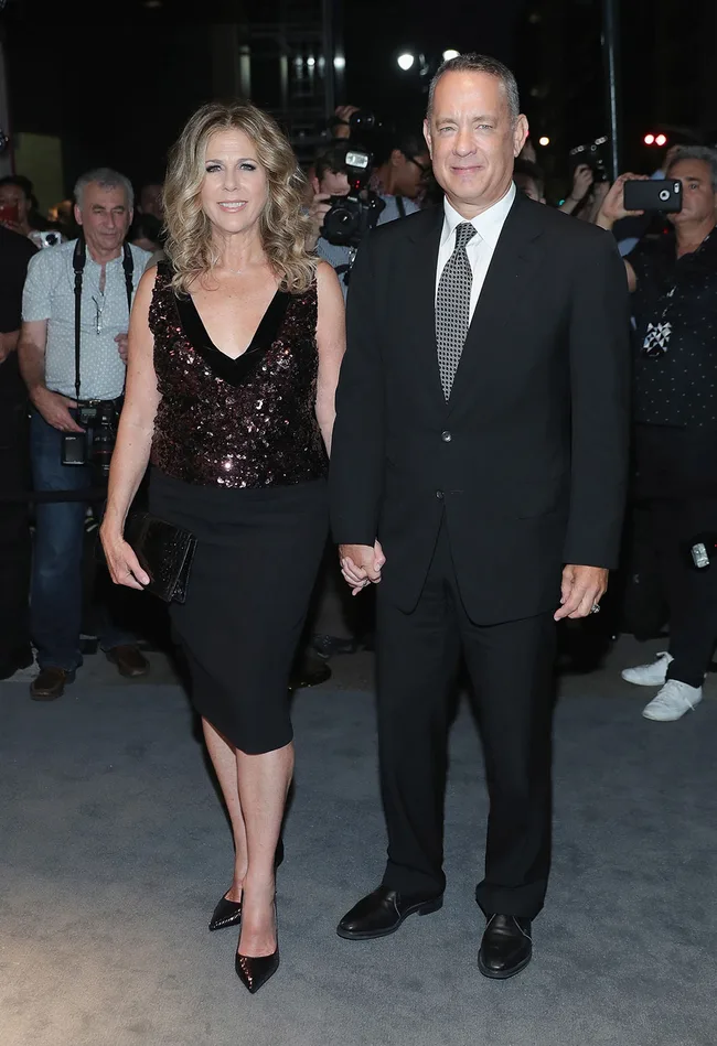 A couple holding hands on a red carpet, with photographers in the background at a formal event.
