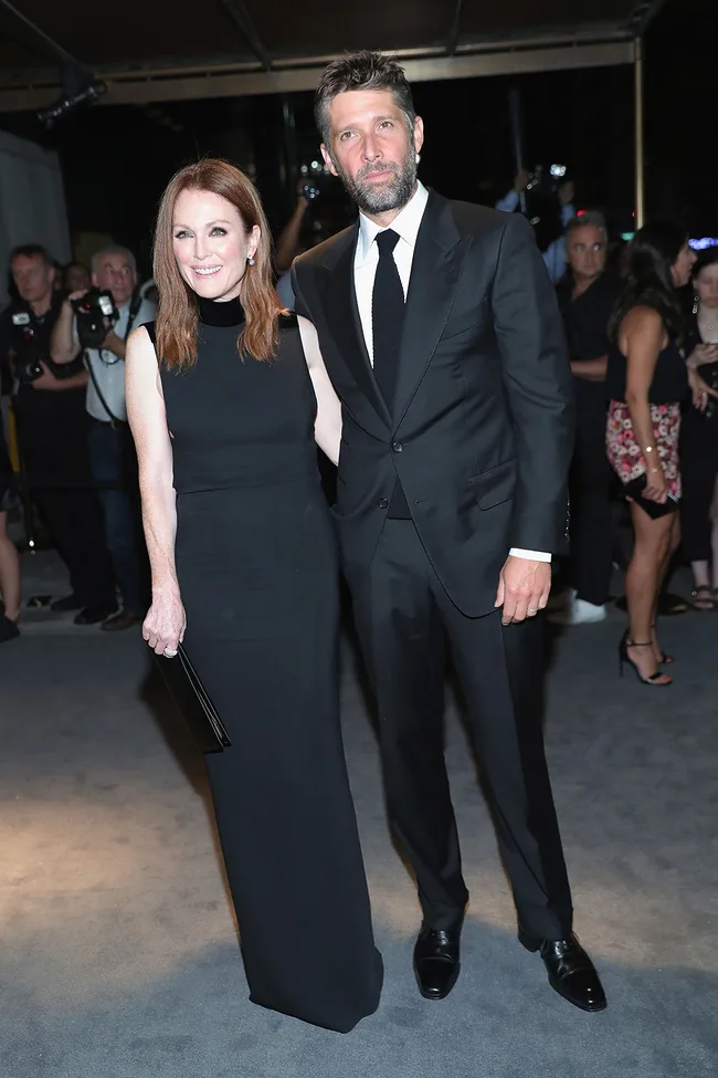 A man and a woman pose together on the red carpet, both in formal black attire, with photographers in the background.