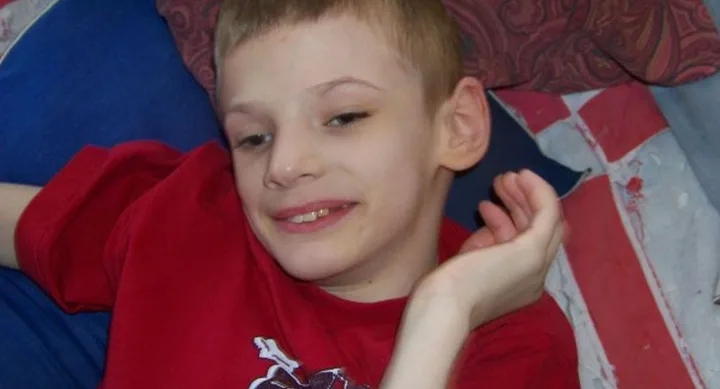 Boy in a red shirt smiling, resting on a couch with a patterned background.
