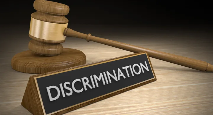 Gavel resting beside a plaque with the word "Discrimination" on a wooden surface.