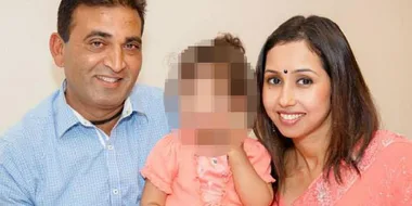 Man and woman smiling, sitting with a blurred child in between.