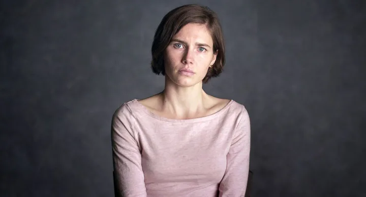 A person with short hair in a light pink top, looking serious against a dark background.