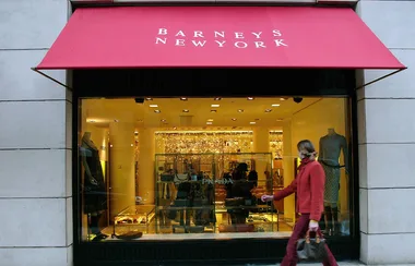 A person walks past a Barneys New York store with a red awning and fashion displays in the window.