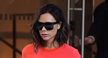 A woman with shoulder-length hair wears large black sunglasses and a bright orange top.