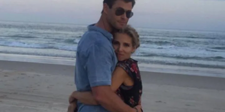 A couple embraces on a sandy beach at sunset, with waves in the background.