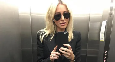 Person with blonde hair, wearing sunglasses, takes a selfie in an elevator mirror.