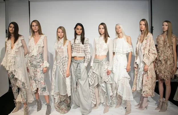 Models in floral and lace outfits with ruffles pose for a fashion show photo.