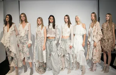 Models in floral and lace outfits with ruffles pose for a fashion show photo.