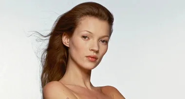A woman with long brown hair poses against a plain background, looking directly at the camera.