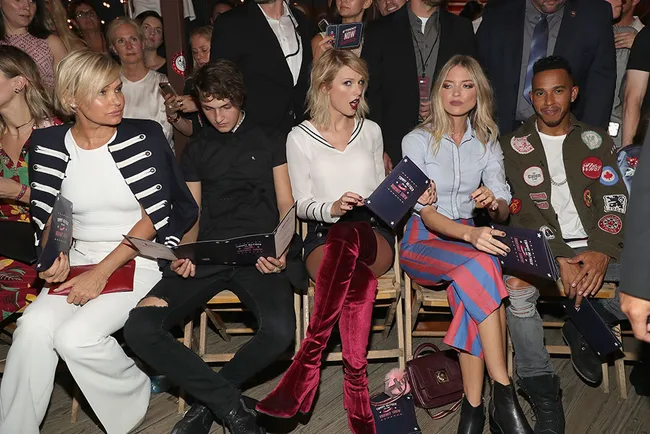 A group of people sitting in a row at an event, holding programs and looking forward.