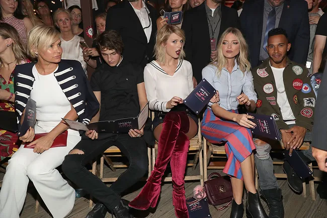 A group of people sitting in a row at an event, holding programs and looking forward.