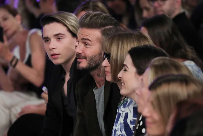 Group of people sitting in a row, attending a fashion show.