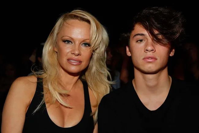 Two people posing together in black clothing at an event, with dark background.