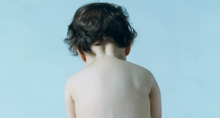 Back of a baby with curly hair against a light blue background.