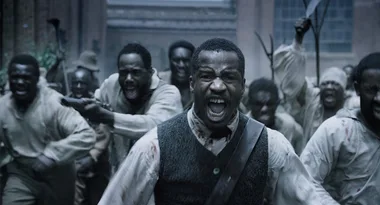 A group of men, led by an angry man in a vest, charge forward in an intense scene from a period film.