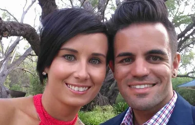 Two people smiling, outdoors with trees in the background.