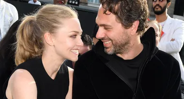 A smiling couple sitting close together, gazing at each other affectionately in an outdoor setting.