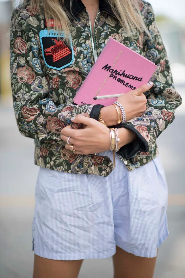 A person in a floral jacket holding a pink book titled "Marihuana Problems."
