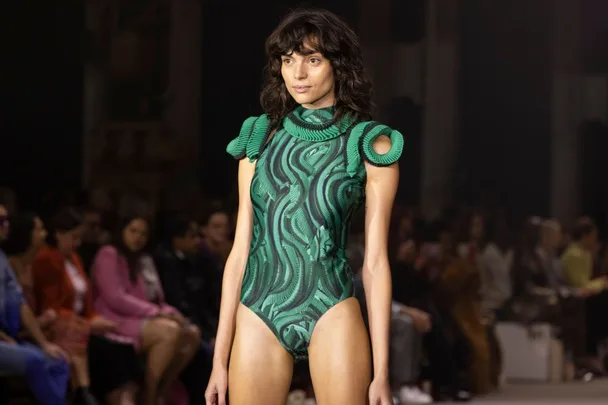 Model walks runway in green, textured bodysuit with looped shoulder details at the Italian Fashion Show, Fall 2023.