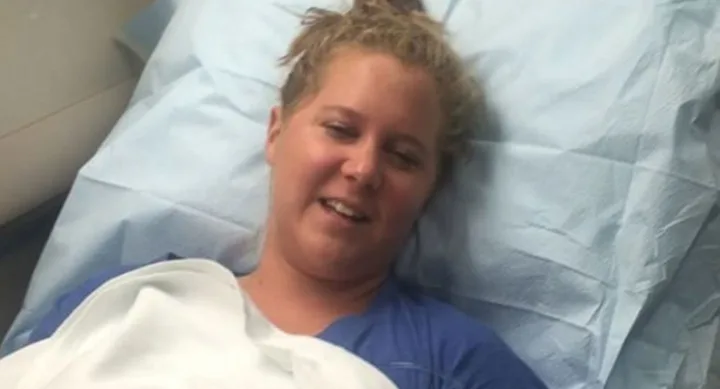 Person smiling while lying in a hospital bed, covered with a light blue sheet.
