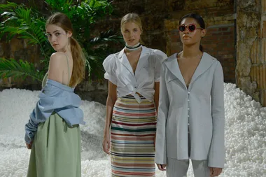 Models pose in eclectic outfits; one in off-shoulder and skirt, another in striped skirt, third in grey suit and sunglasses.