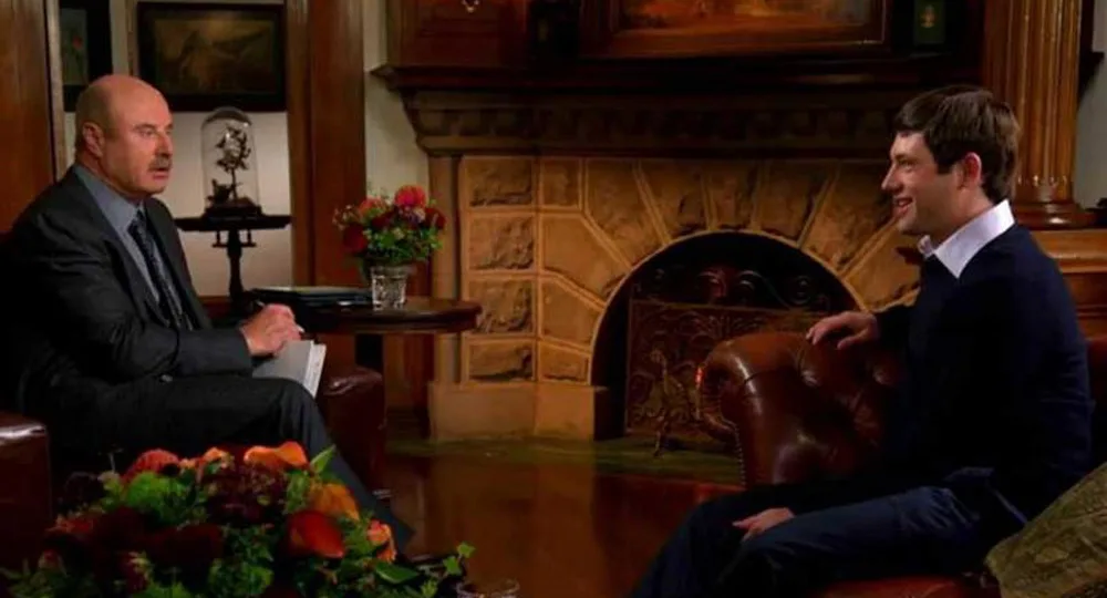 Two men seated and engaged in conversation in a warmly decorated living room setting.