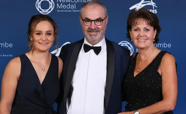 Three people standing together at the Newcombe Medal event; man in tuxedo, women in black dresses, all smiling.