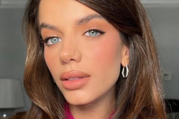 A woman with long brown hair, blue eyes, and wearing silver earrings poses for a close-up photo, with a neutral expression.