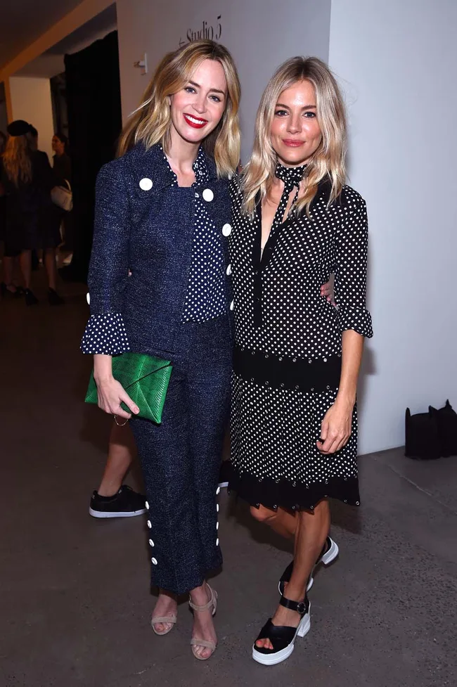Two women in stylish outfits pose together; one holds a green clutch.