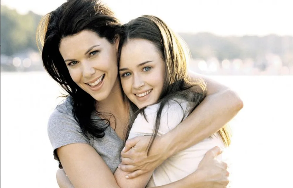 Mother and daughter hugging happily by a lakeside.