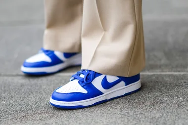 Close-up of beige pants and blue-and-white Nike sneakers on a grey pavement.