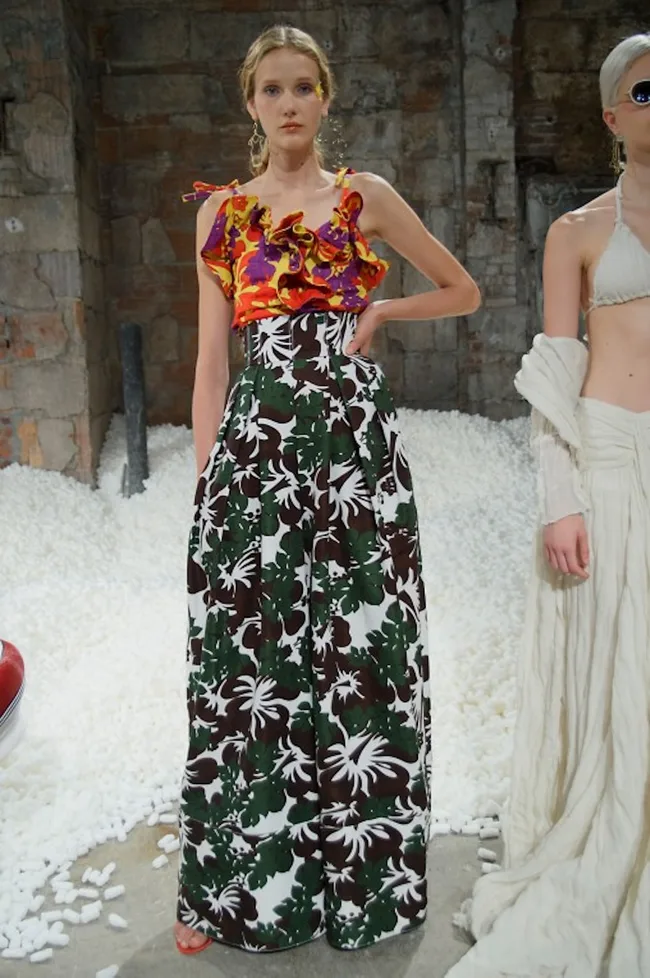 Model wearing colorful floral top and tropical print skirt at a fashion show.