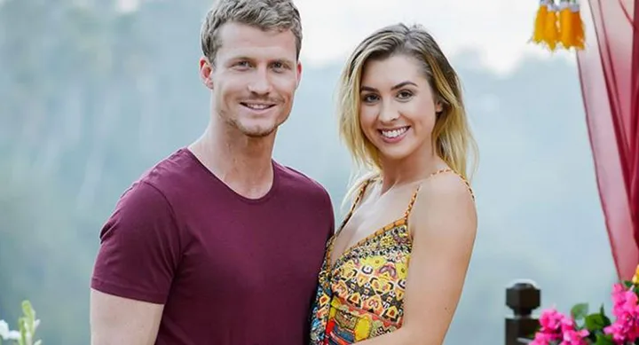 Man and woman smiling outdoors, standing closely with a scenic background.
