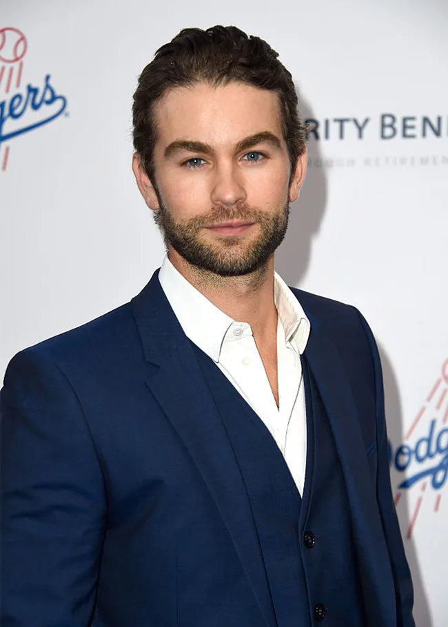 Man in a blue suit and white shirt at an event with a Dodgers logo backdrop, smiling slightly at the camera.